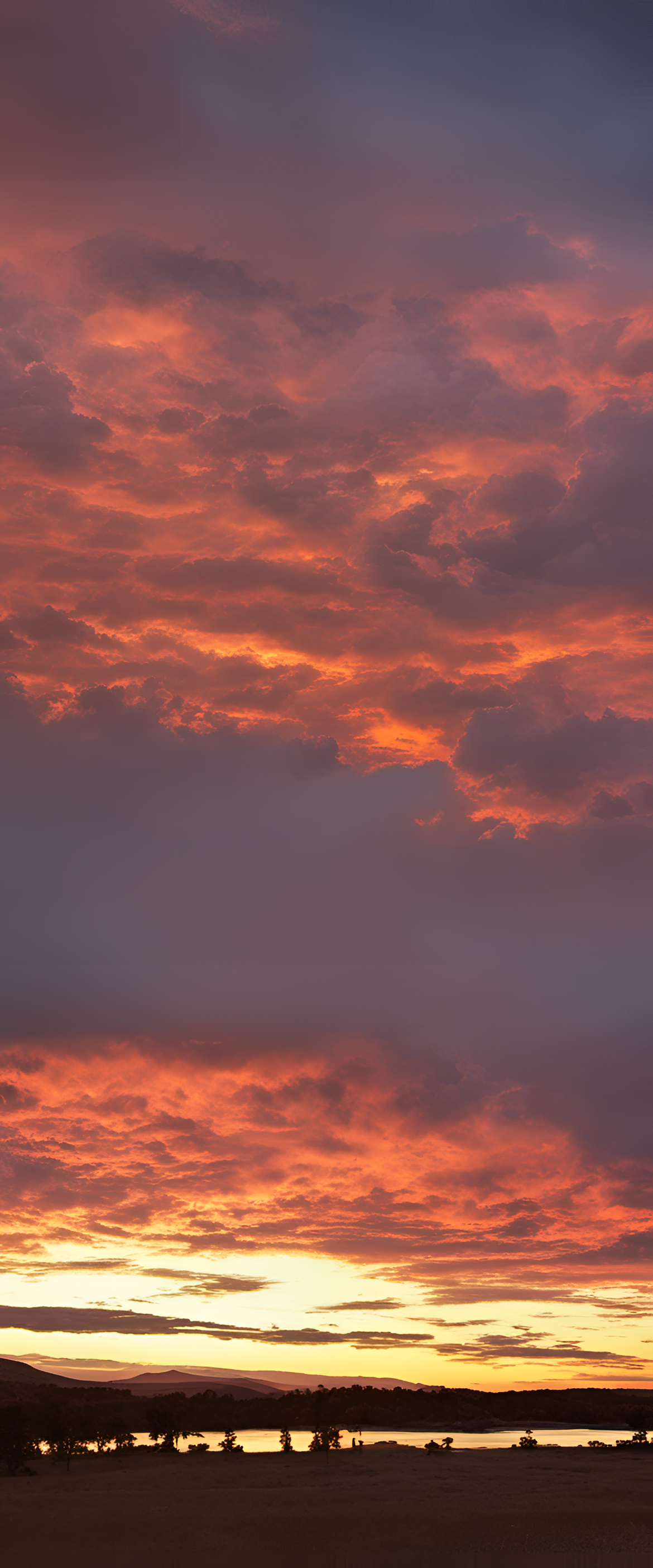 Vibrant sunset sky illuminates the horizon with warm hues and clouds casting soft pink reflections.